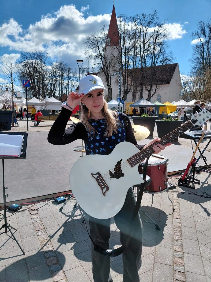A Lindo player holding a White Dove acoustic guitar at an outdoor music event.