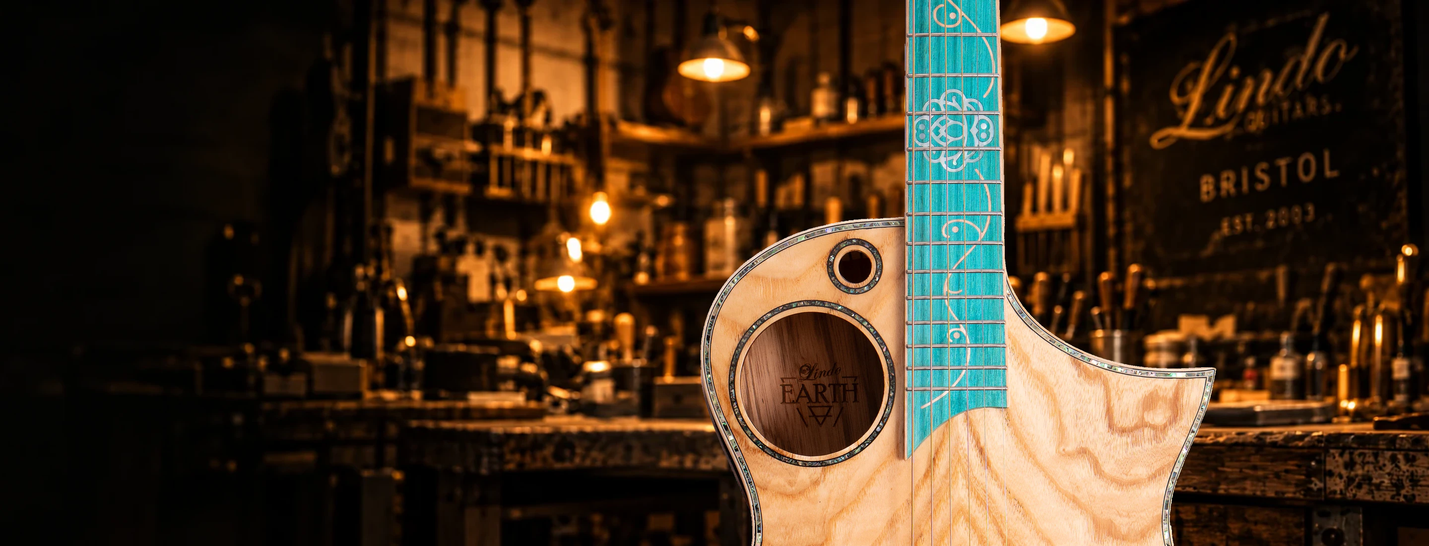 A close-up of the Lindo Earth V2 guitar against the warmly lit Lindo workshop